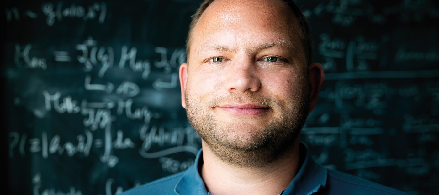 A man stands in front of a blackboard with equations