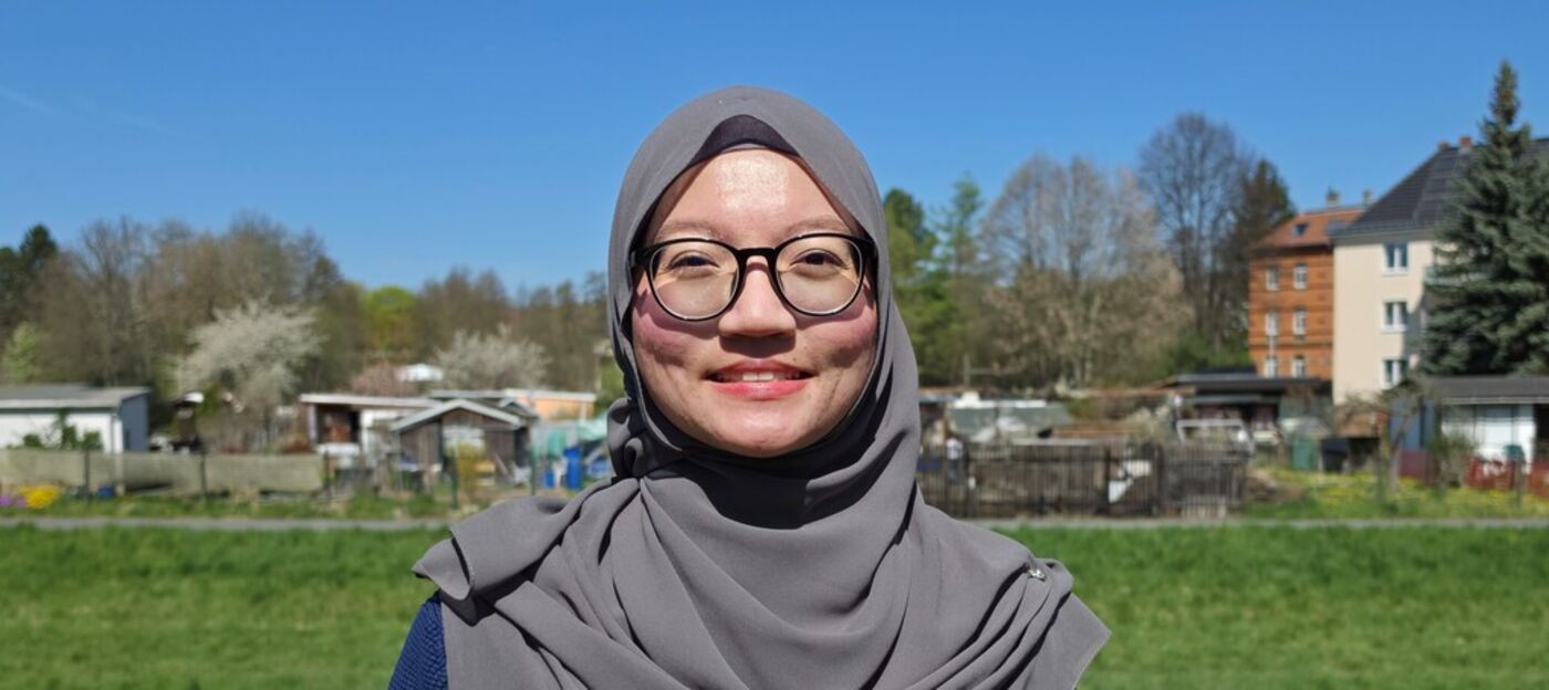 Frau mit Brille und Kopftuch vor einer Gartenanlage